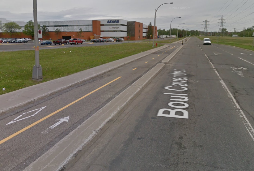 Avec un magasin Sears en arrière-plan, une piste cyclable à gauche d'un boulevard.